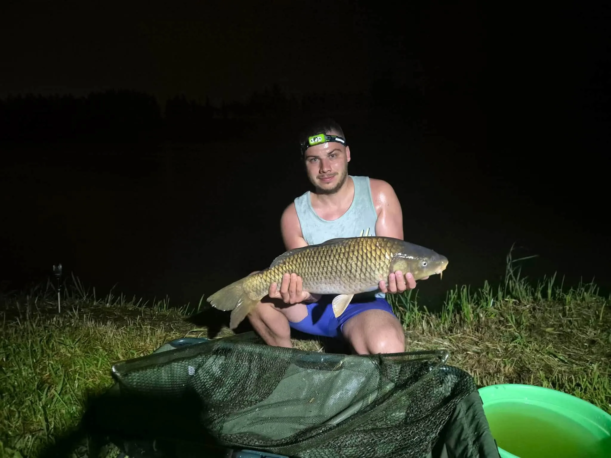 Nocna zasiadka — wędkarz z czołówką trzyma karpia